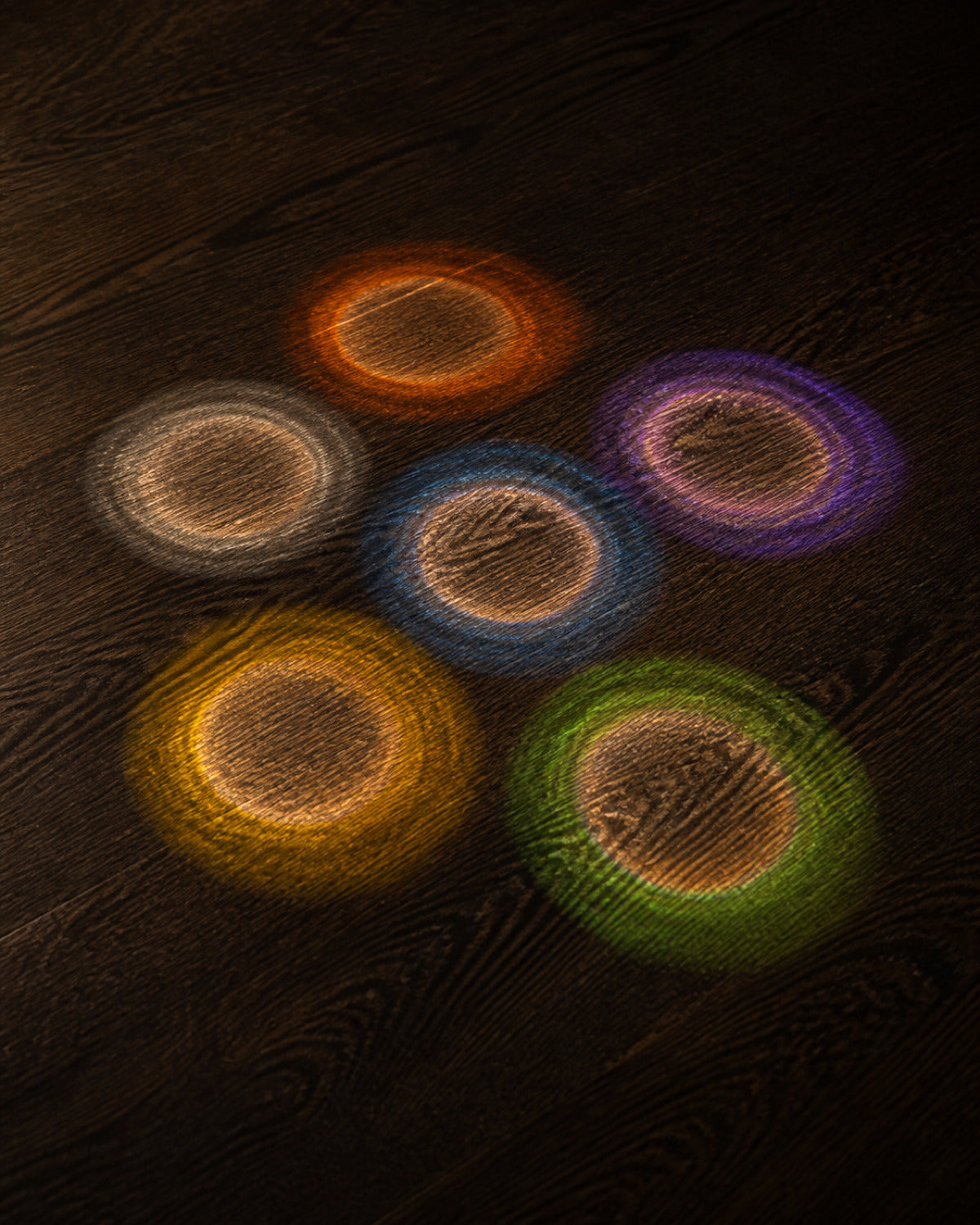 Six pools of light on dark oak, each with a clear centre ringed in colour.