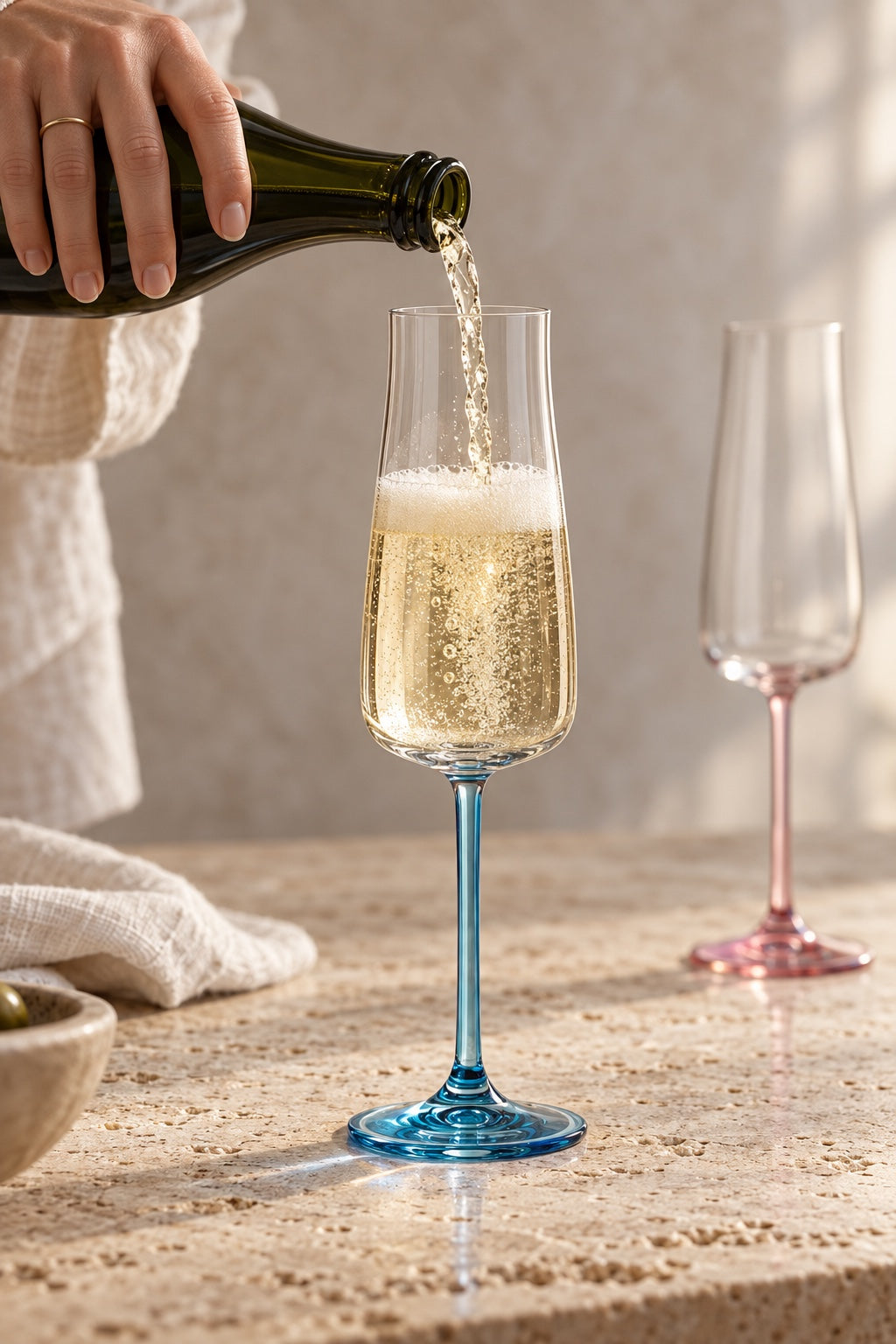 Champagne being poured into a Poppy flute with a blue stem on a travertine counter